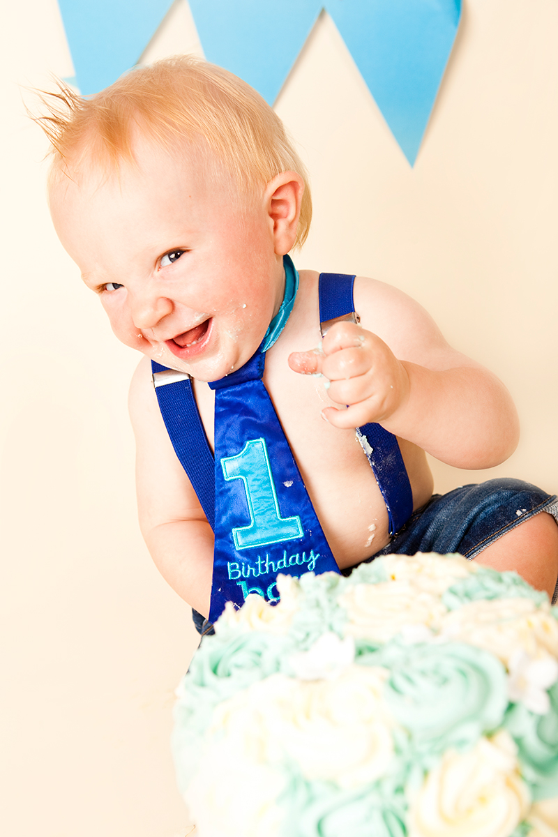 Cheeky baby boy sitting behind his birthday cake wearing blue tie. 