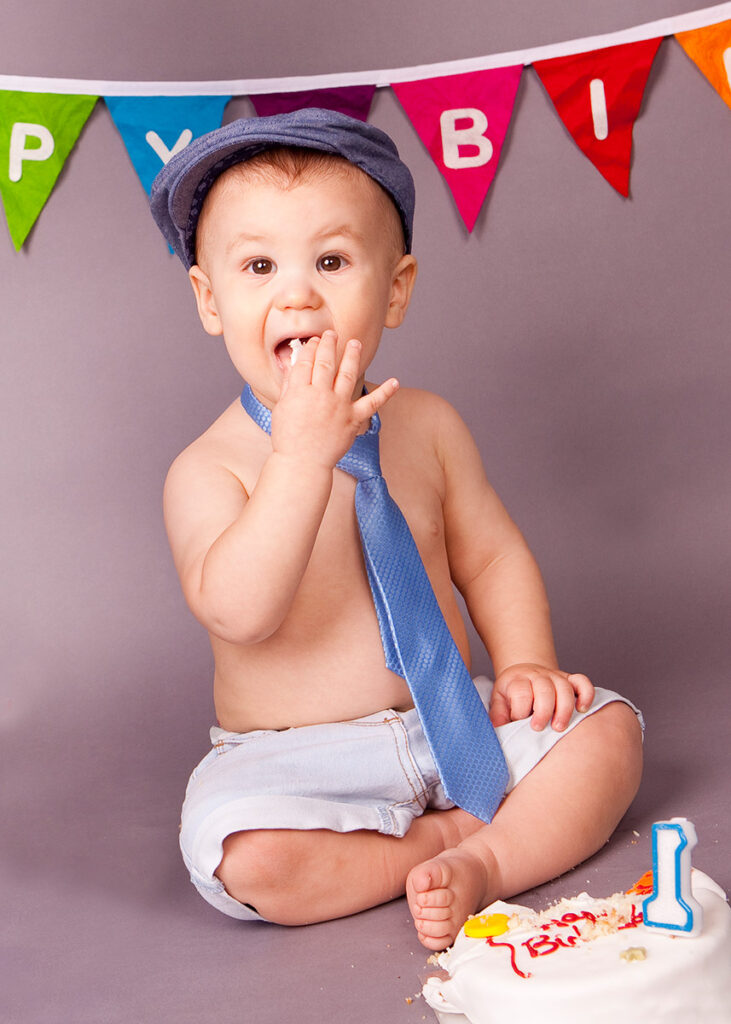 One year old baby is shoving his birthday cake into his mouth during his cake smash session.
