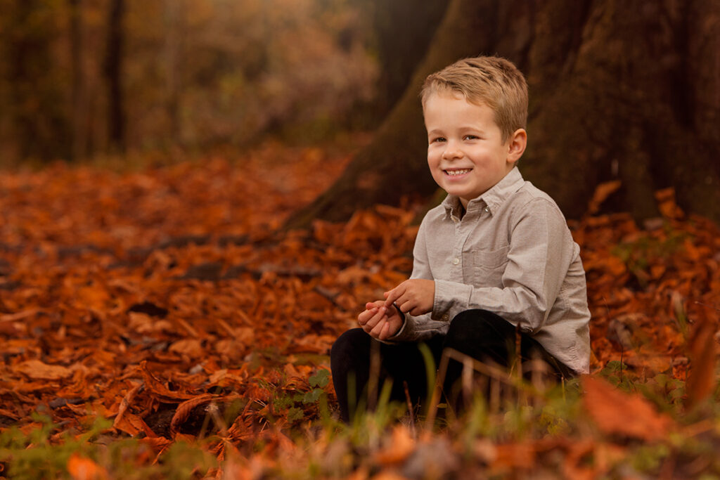 A boy smiling at the photographer. You can see autumn background. 