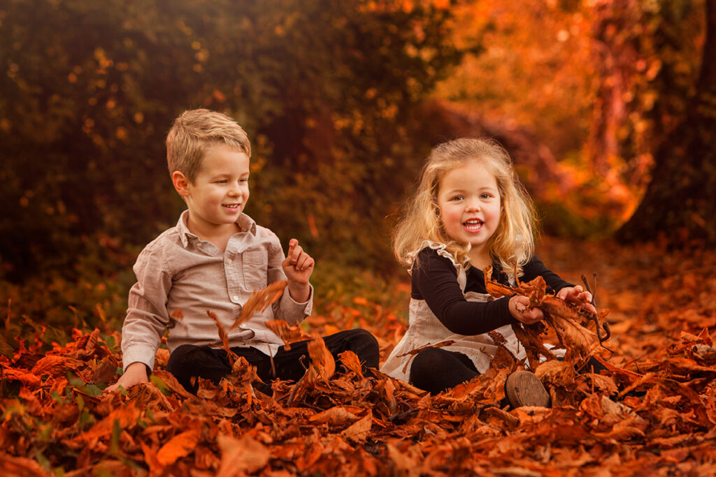 A boy and a girl are sitting on autumn leaves. 