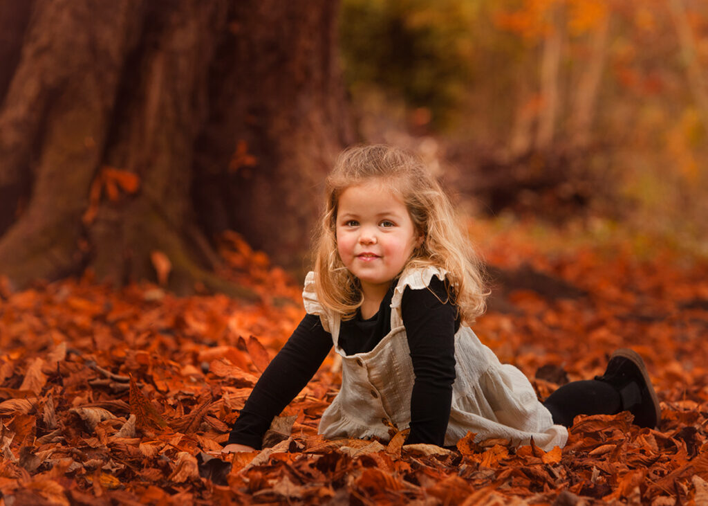 Girl laying on her tummy on a pile of autumn leaves. 