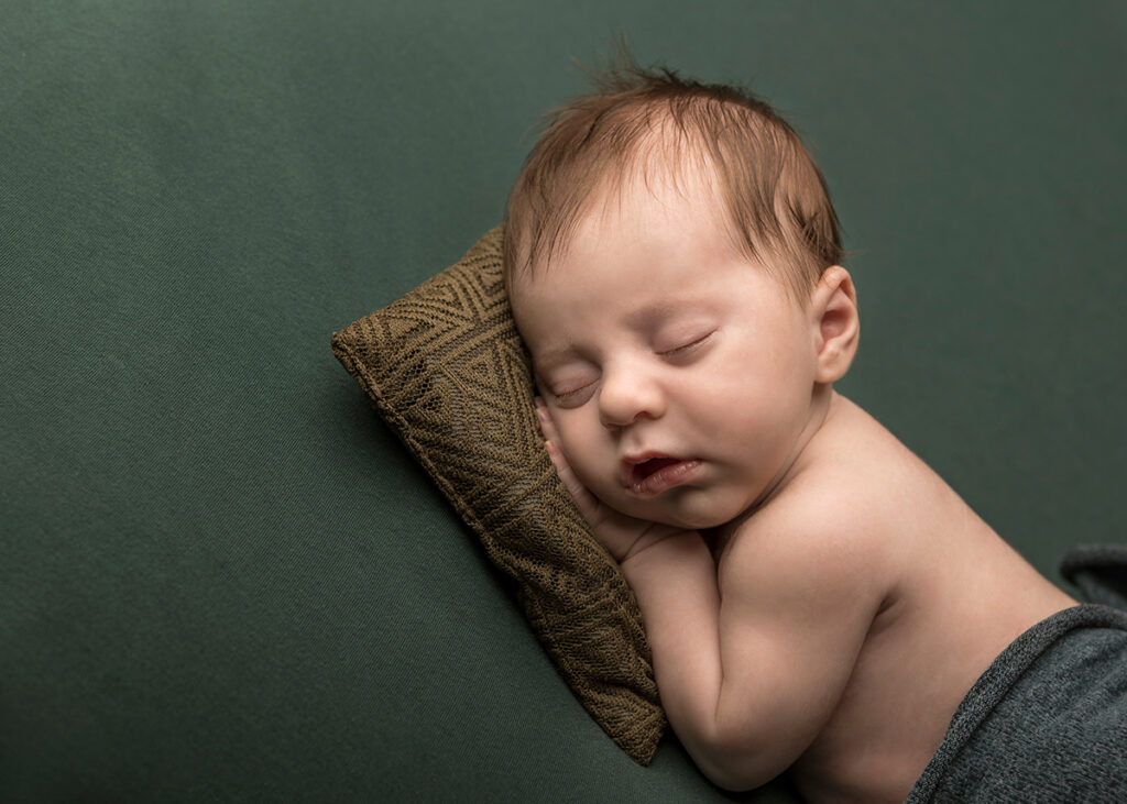 Newborn boy sleeping on a green pillow during his photo shoot.