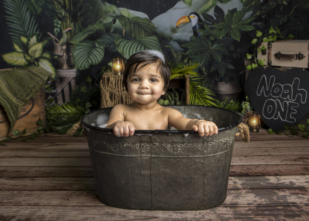 Noah is in a bath tub after his cake smash session in a jungle themed cake smash session.